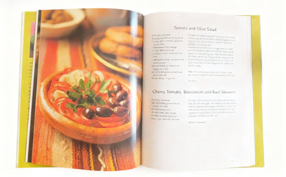 Open cookbook showing a recipe for Tomato and Olive Salad with an image of the dish on the left page.